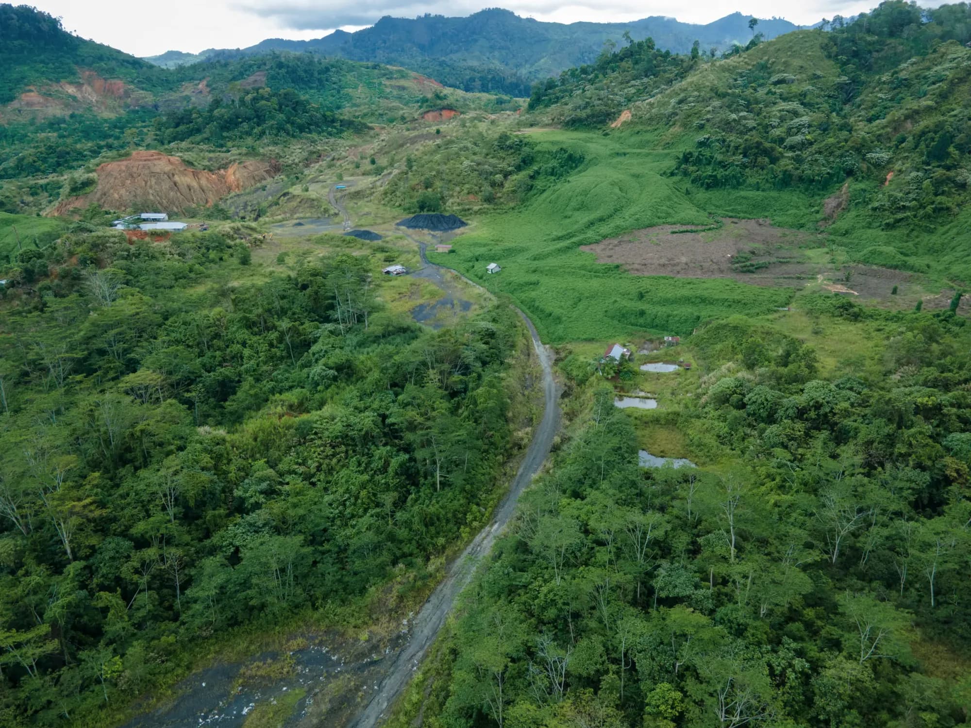 Aerial view of a haul road winding through forested hills toward a mine area and stockpile