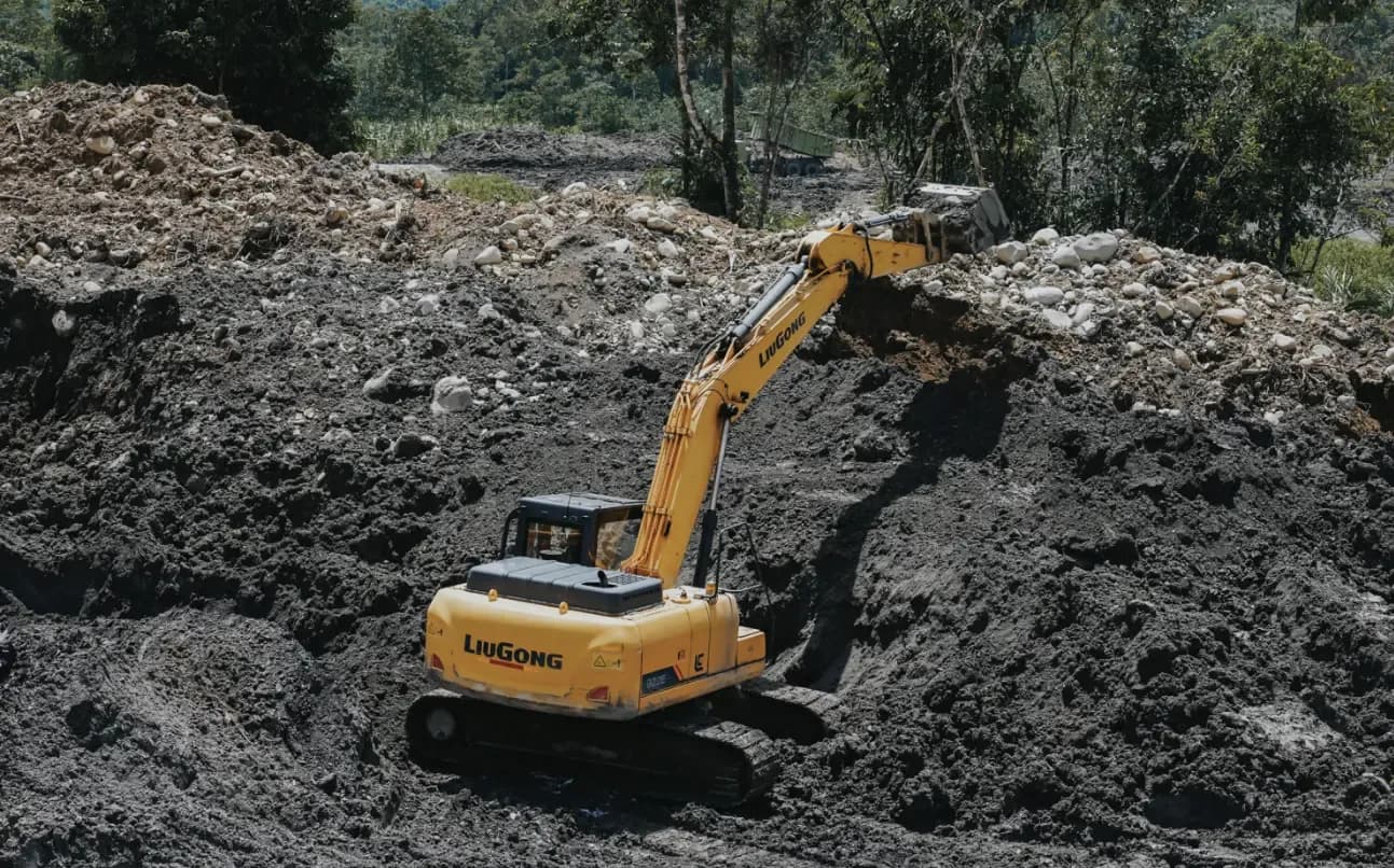 Tracked excavator working a coal stockpile with forest behind